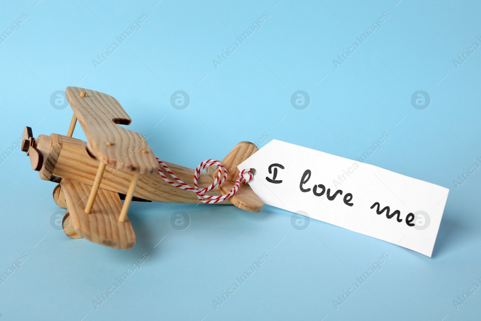 Photo of Tag with handwritten phrase I Love Me and wooden airplane on turquoise background
