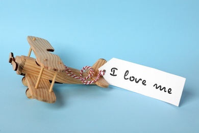 Tag with handwritten phrase I Love Me and wooden airplane on turquoise background