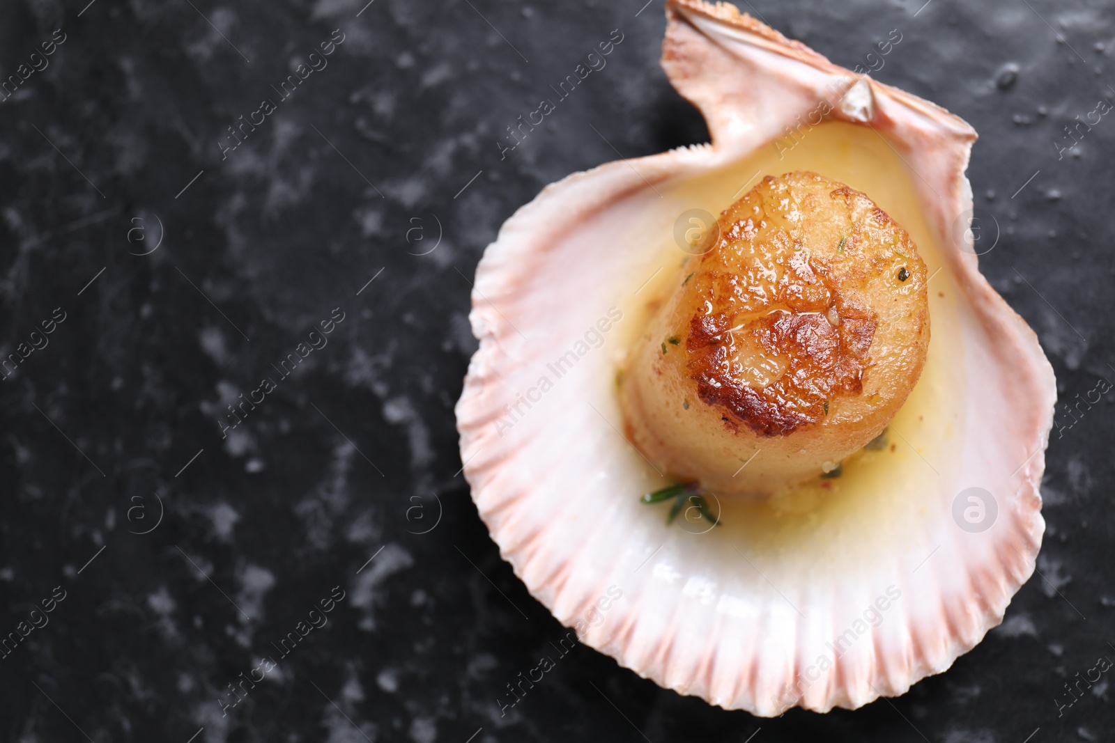 Photo of Delicious fried scallop in shell on black table, top view. Space for text