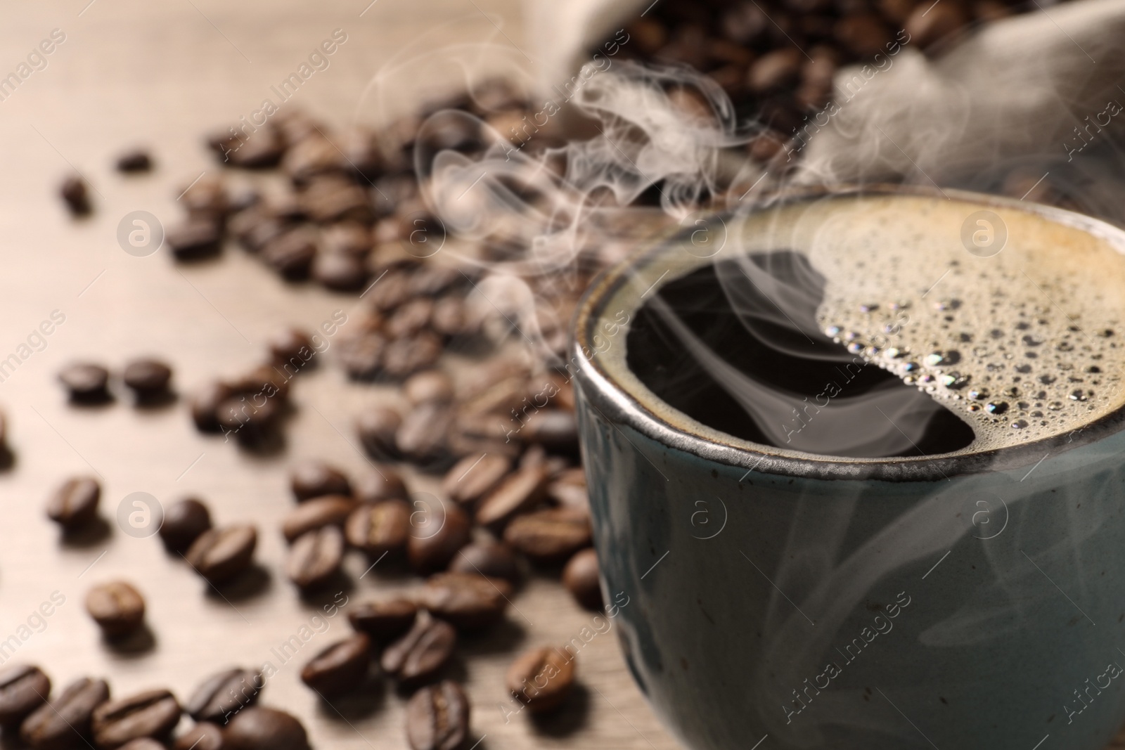 Image of Cup of aromatic hot coffee and beans on wooden table, closeup. Space for text