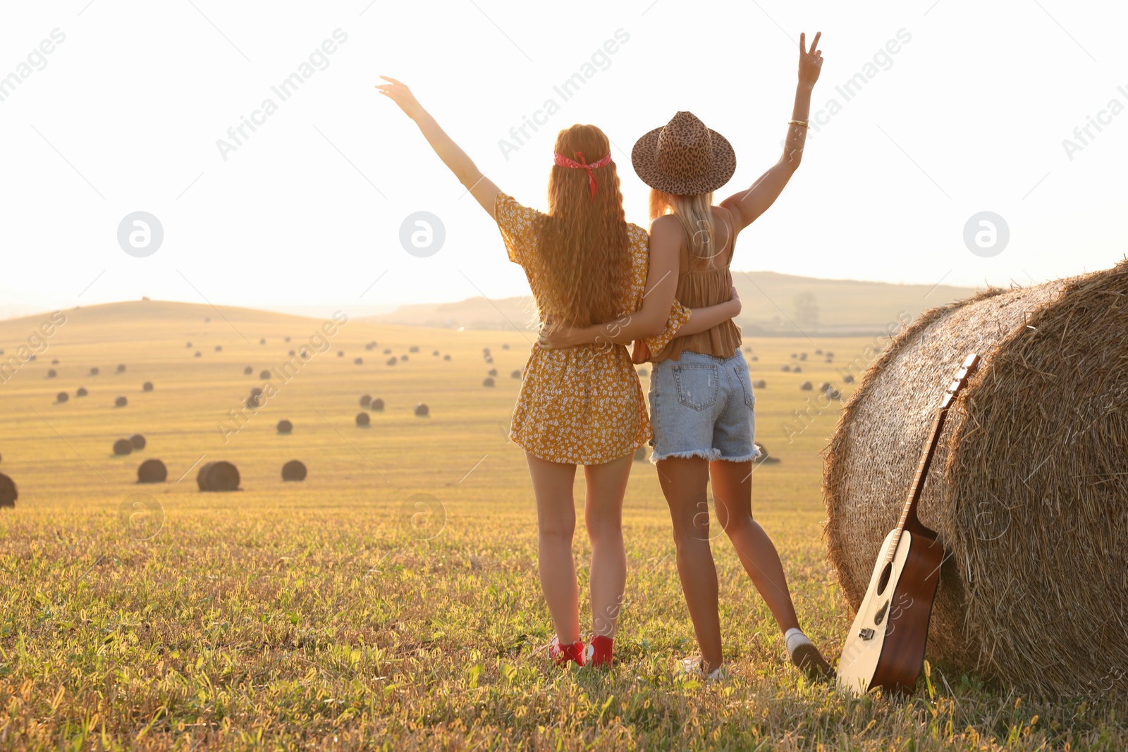 Photo of Hippie women near hay bale in field, back view