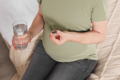 Pregnant woman taking pill on bed, closeup