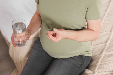 Photo of Pregnant woman taking pill on bed, closeup