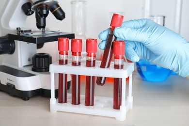 Image of Scientist taking test tube with blood sample from rack at table, closeup. Laboratory analysis