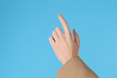 Photo of Businesswoman pointing at something on light blue background, closeup. Finger gesture