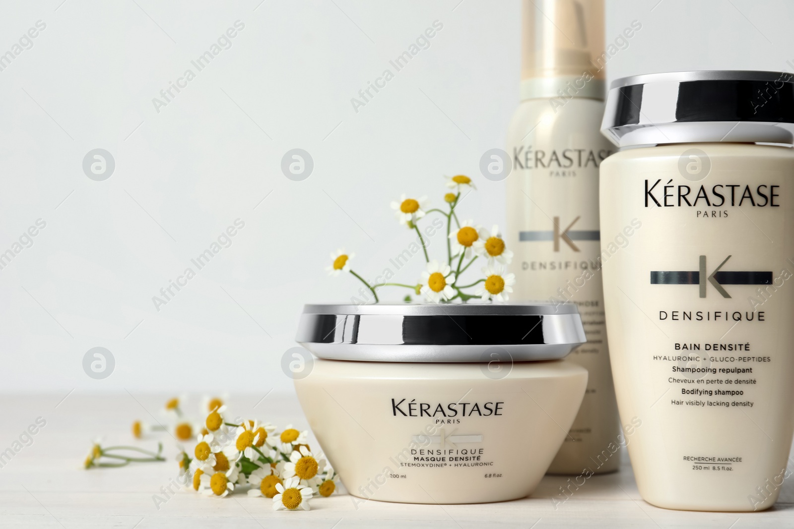 Photo of MYKOLAIV, UKRAINE - SEPTEMBER 07, 2021: Set of Kerastase hair care cosmetic products and chamomile flowers on white wooden table. Space for text