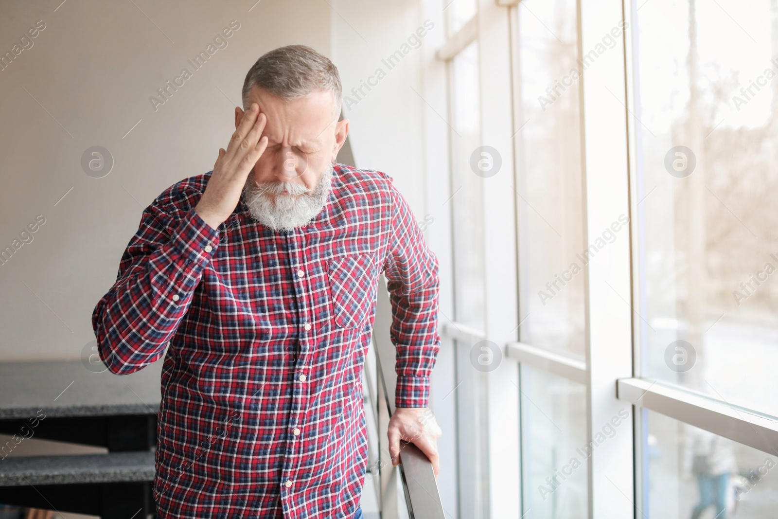 Photo of Mature man suffering from headache near window in office