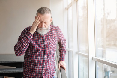 Photo of Mature man suffering from headache near window in office