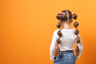 Photo of Little girl with beautiful hairstyle on orange background, back view. Space for text