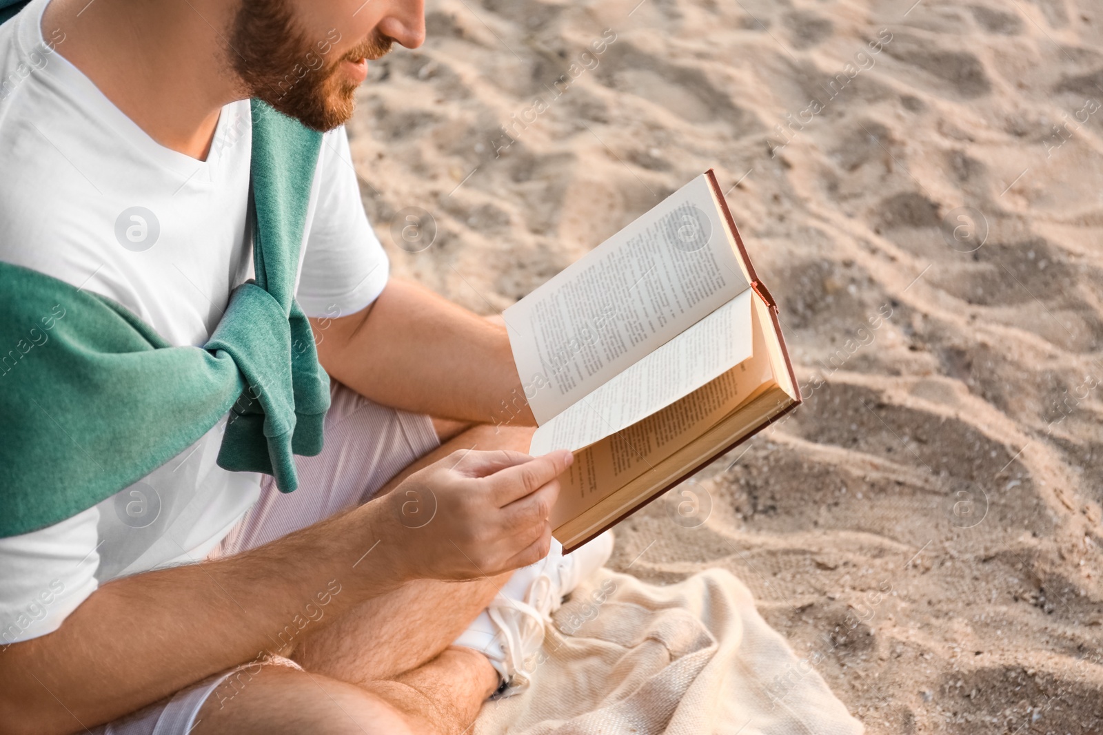 Photo of Young man reading book on sandy beach, closeup