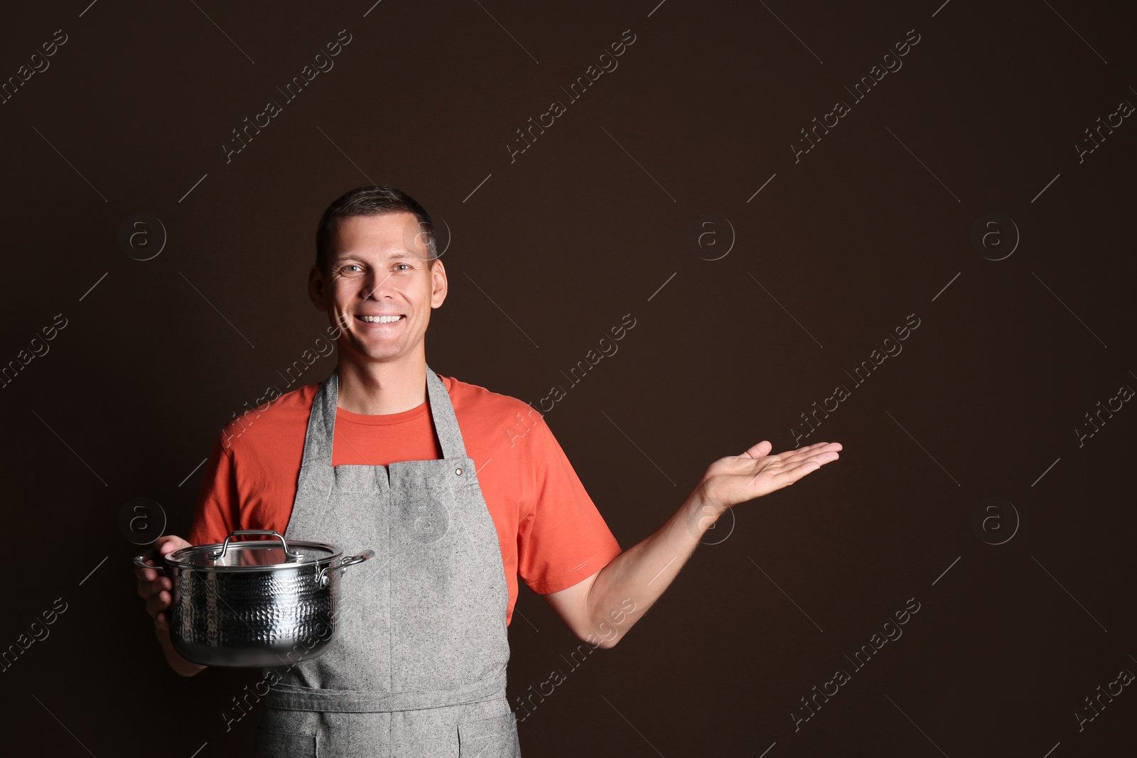 Photo of Happy man with cooking pot on brown background. Space for text