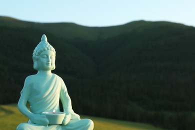 Decorative Buddha statue with burning candle in mountains, closeup. Space for text