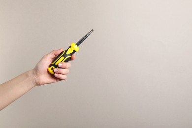 Photo of Woman holding screwdriver on grey background, closeup. Space for text