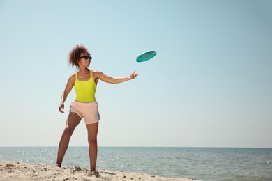 Happy African American woman catching flying disk at beach on sunny day