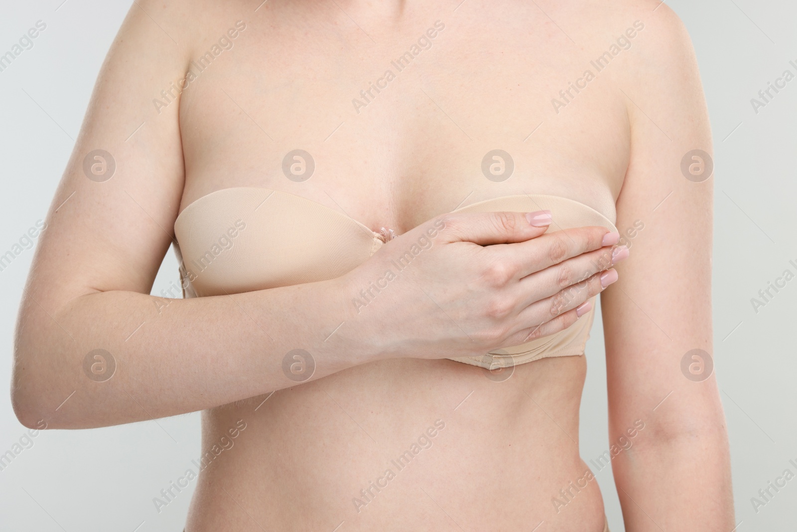 Photo of Mammology. Young woman doing breast self-examination on light grey background, closeup