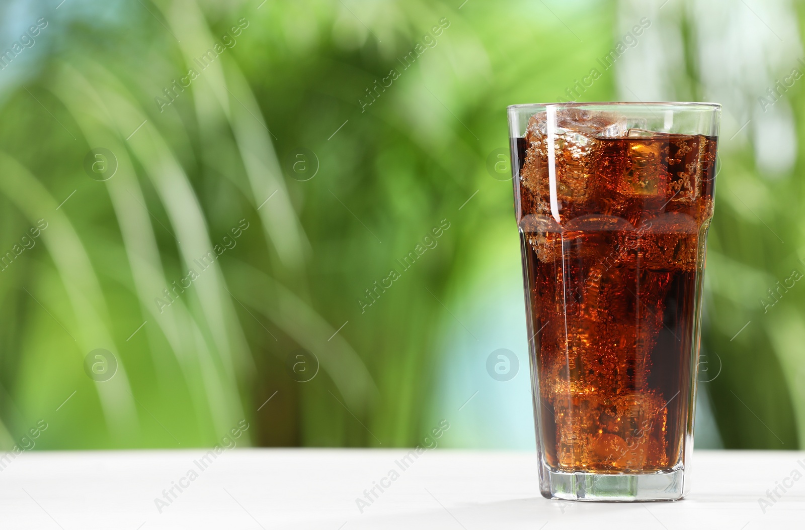 Photo of Glass of refreshing soda water with ice cubes on white table outdoors, space for text