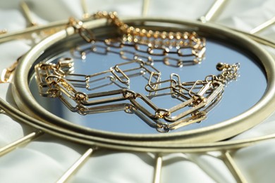 Metal chains and mirror on white fabric, closeup. Luxury jewelry