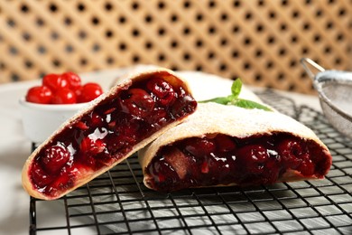 Photo of Delicious strudel with cherries on cooling rack, closeup