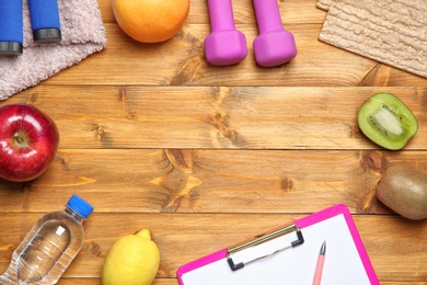 Flat lay composition with sport items, healthy food, clipboard and space for text on wooden background. Weight loss concept