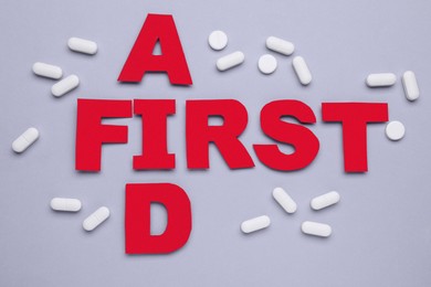 Words First Aid made of red letters and pills on grey background, flat lay