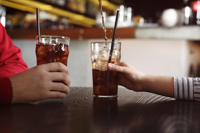 Couple with glasses of  cola at table indoors, closeup. Pouring refreshing beverage