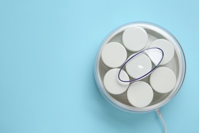 Photo of Modern yogurt maker with jars on light blue background, top view. Space for text