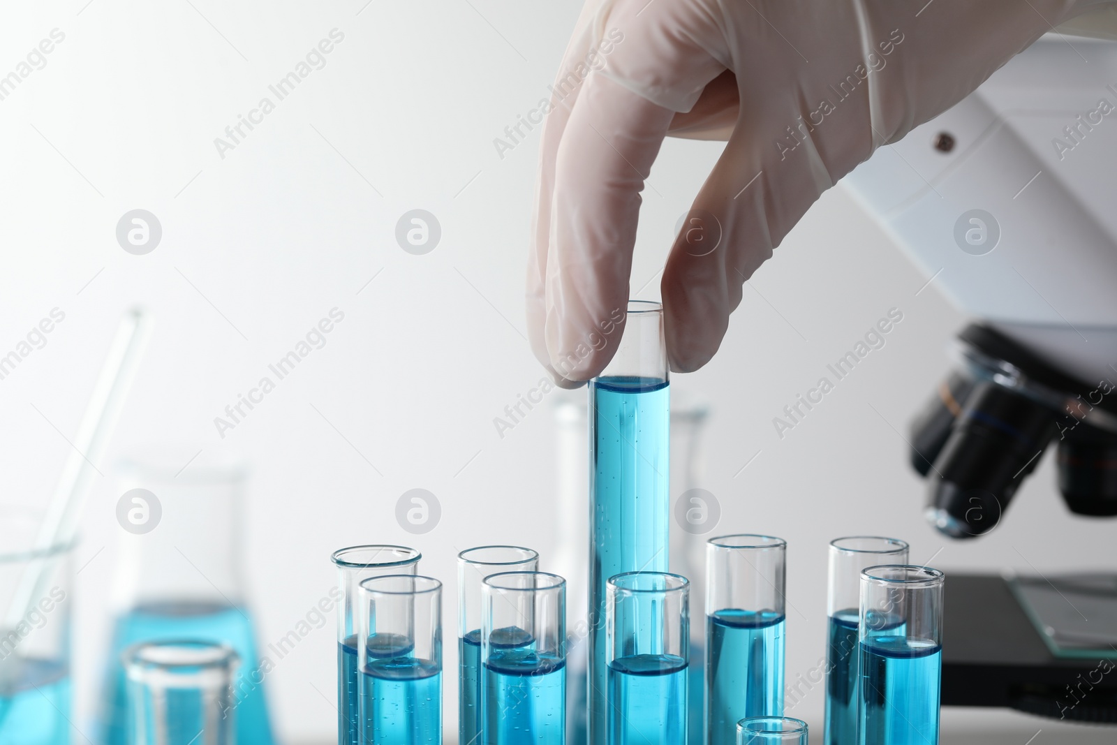 Photo of Scientist taking test tube with light blue liquid in laboratory, closeup