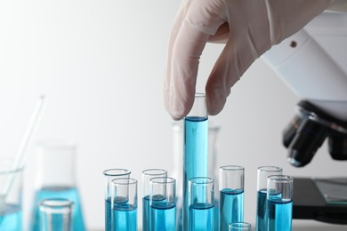 Scientist taking test tube with light blue liquid in laboratory, closeup