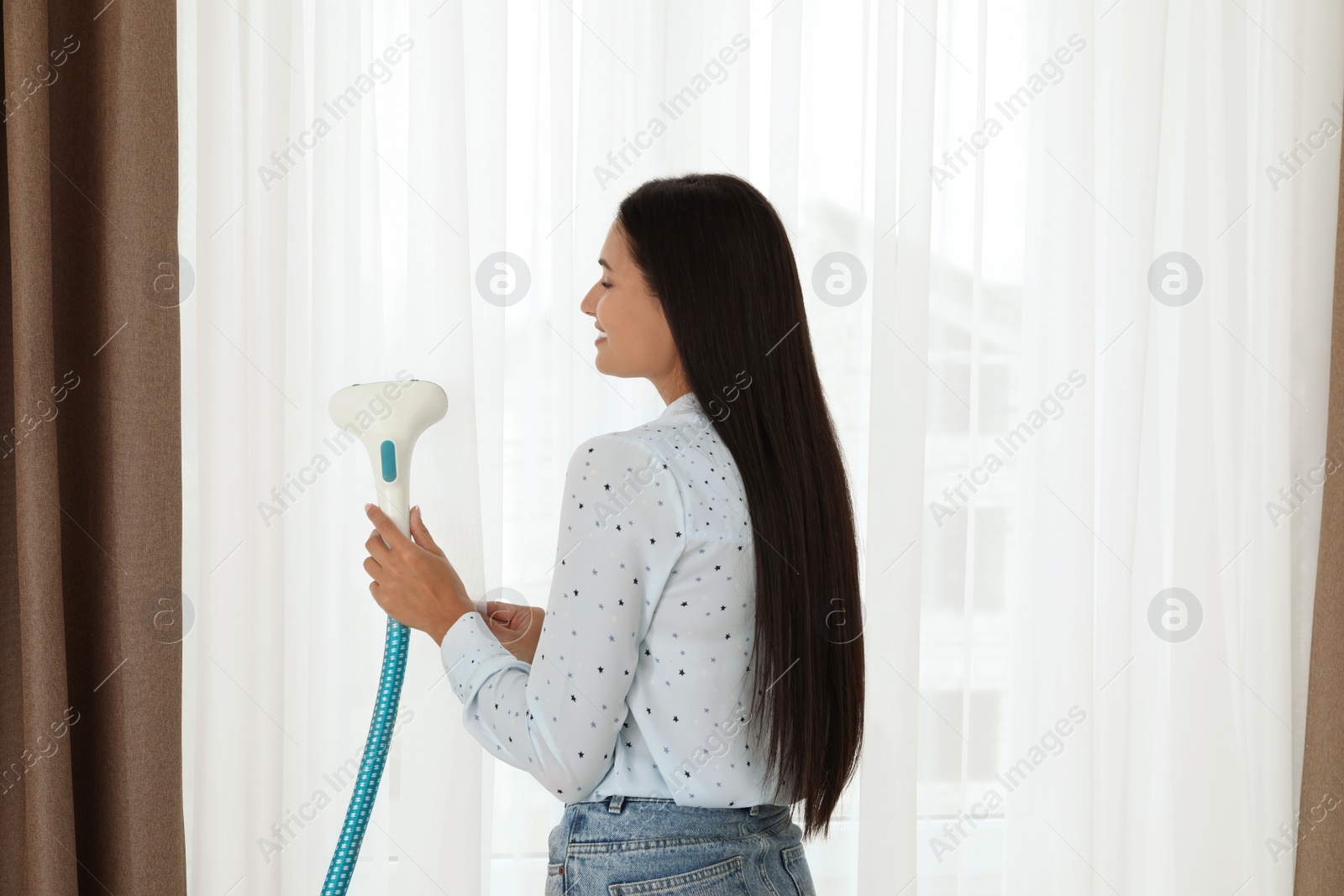 Photo of Woman steaming curtain near window at home