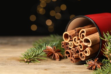 Many cinnamon sticks, anise stars and fir branches on wooden table, closeup. Space for text