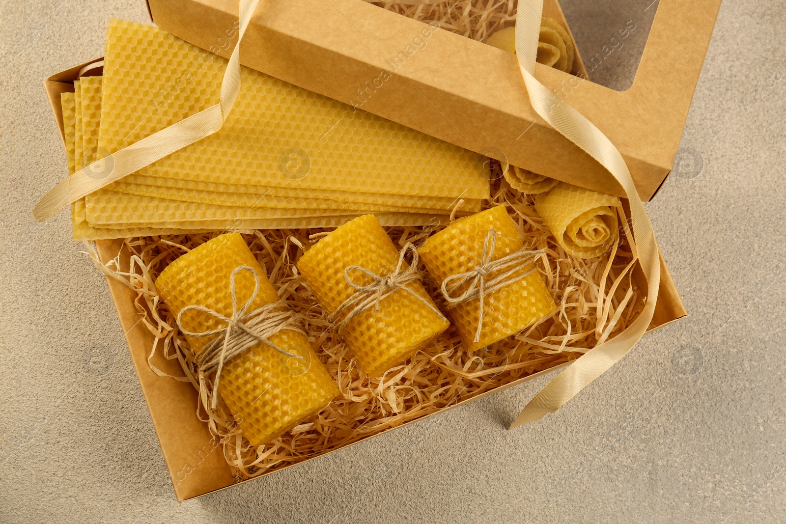 Photo of Beautiful yellow beeswax candles and sheets in box on light textured table, top view