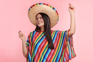 Photo of Young woman in Mexican sombrero hat and poncho dancing on pink background