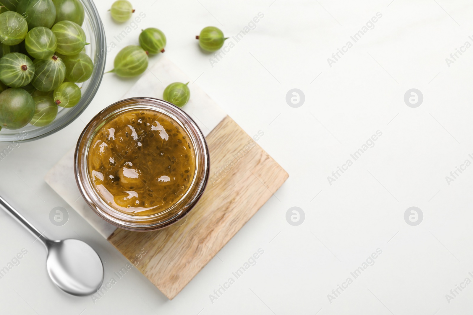 Photo of Jar of delicious gooseberry jam and fresh berries on white table, flat lay. Space for text