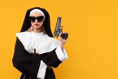 Photo of Woman in nun habit and sunglasses holding handgun against orange background, space for text