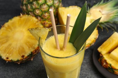 Photo of Tasty pineapple smoothie and fruit on grey table, closeup