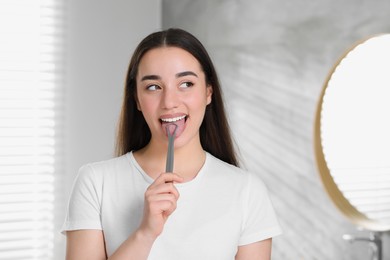 Photo of Happy woman brushing her tongue with cleaner in bathroom