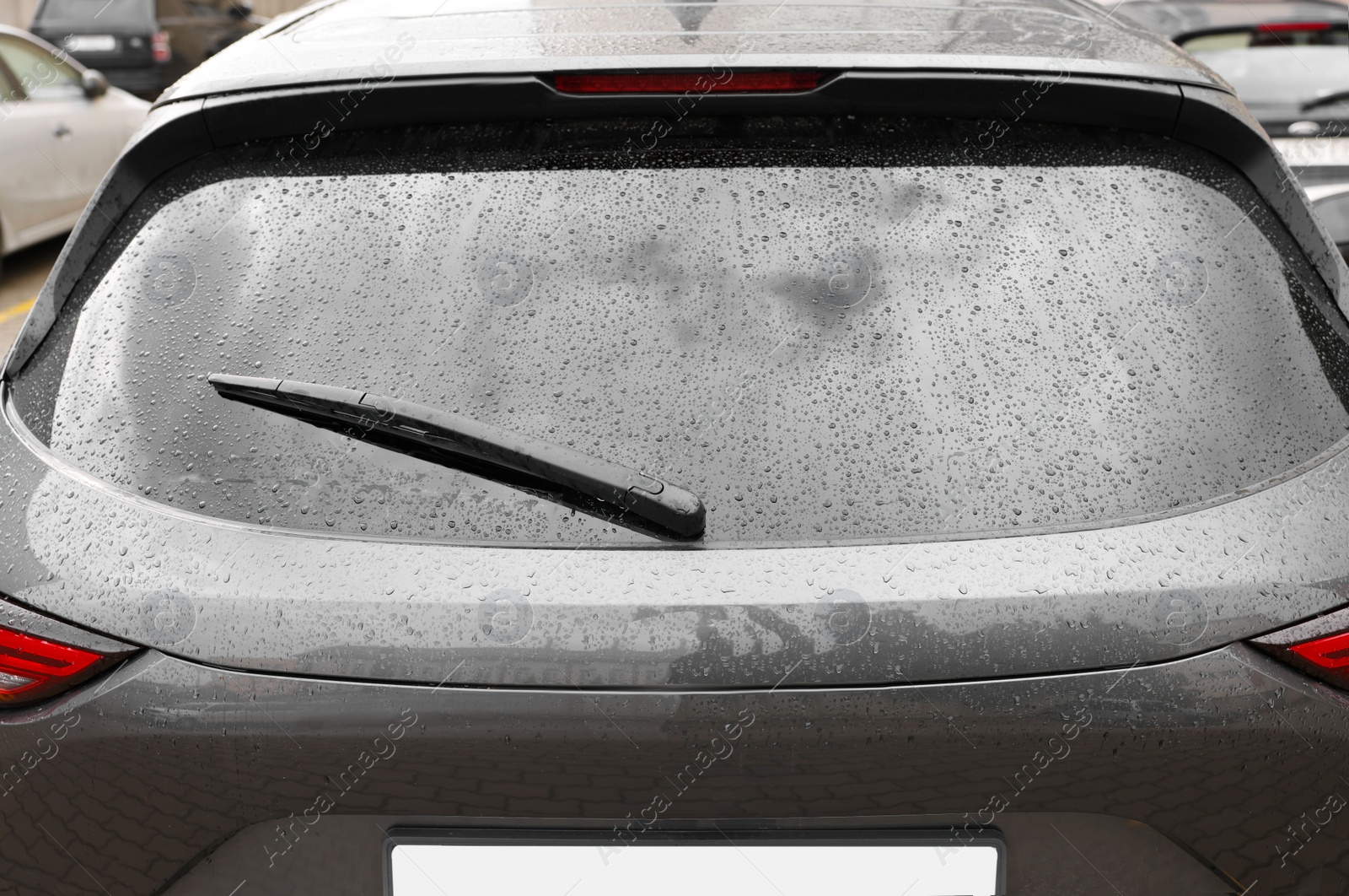 Photo of Car wiper cleaning water drops from rear windshield glass outdoors, closeup