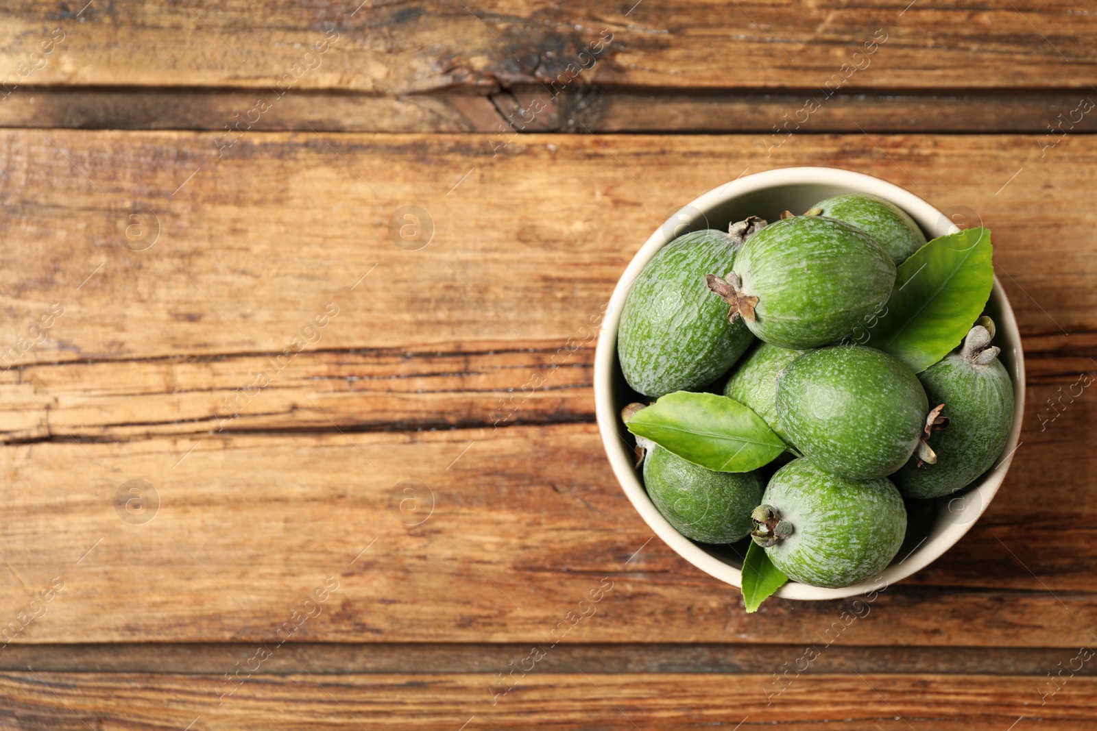 Photo of Fresh green feijoa fruits in bowl on wooden table, top view. Space for text