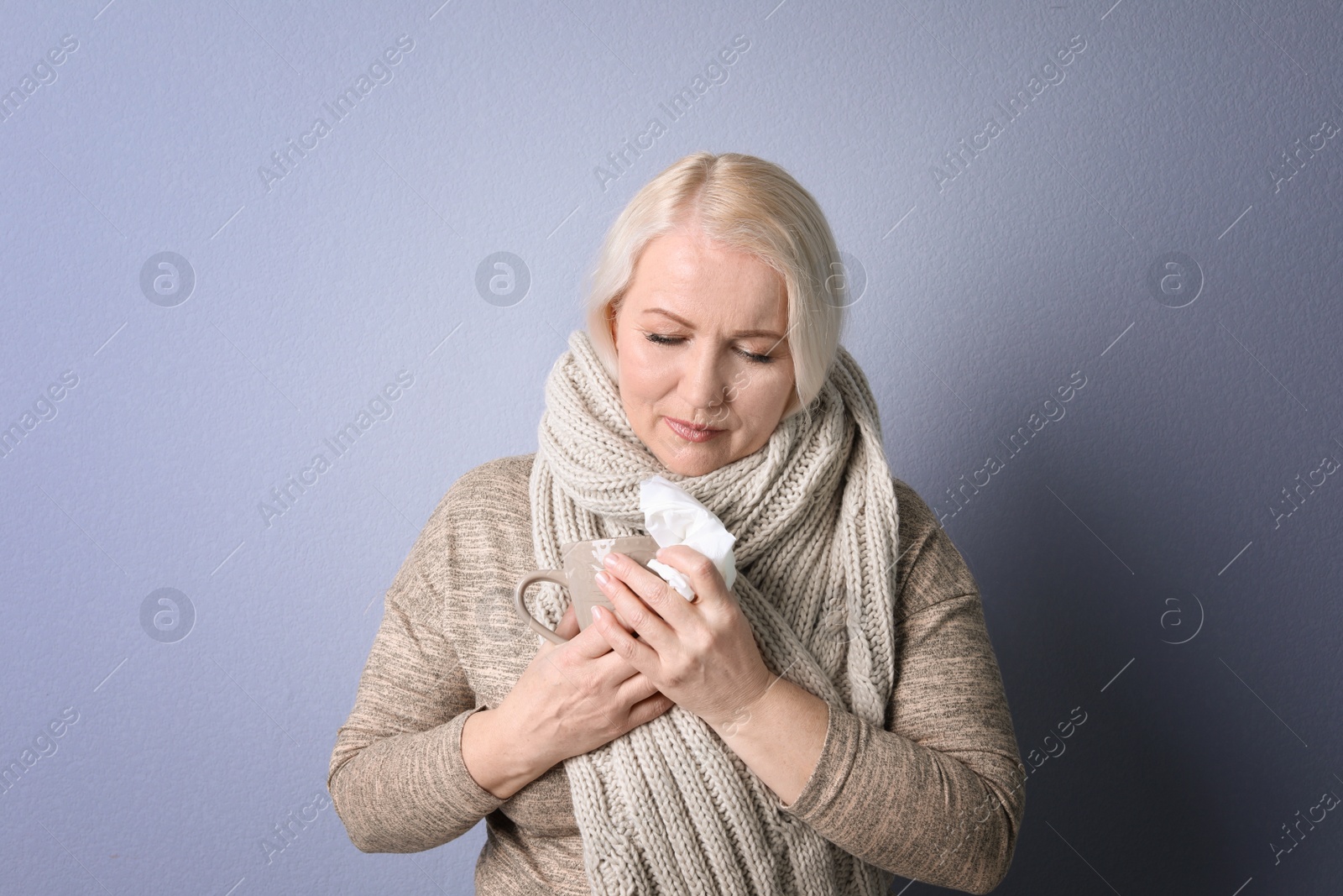 Photo of Mature woman with tissue suffering from cold on color background