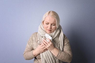 Mature woman with tissue suffering from cold on color background