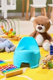 Light blue baby potty, teddy bear and many other toys in room. Toilet training