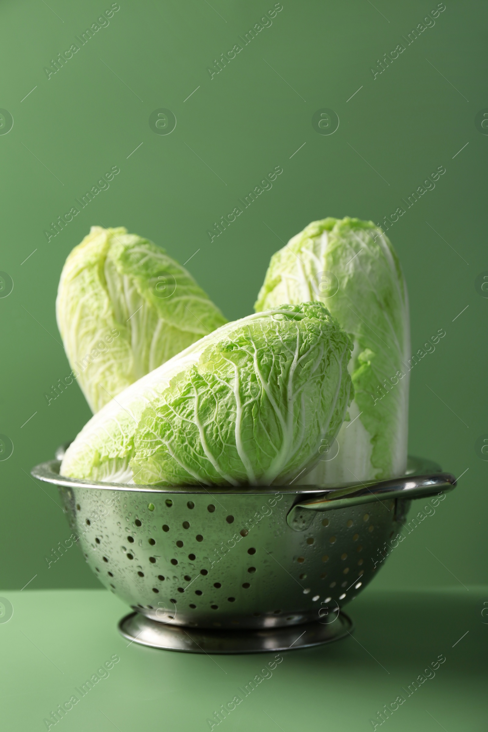 Photo of Fresh Chinese cabbages in colander on green background