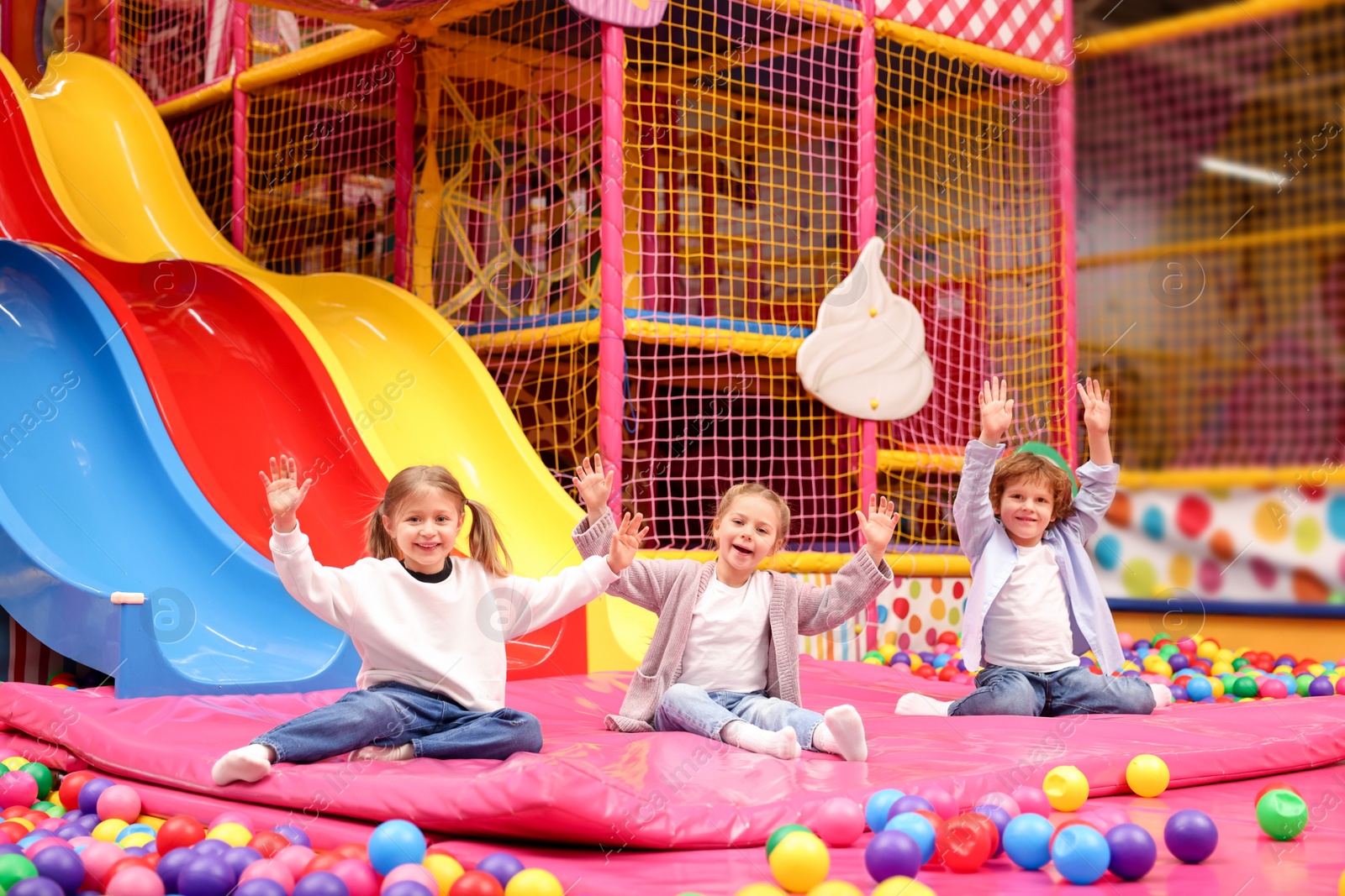 Photo of Happy kids playing in play room with slides, mats and ball pit