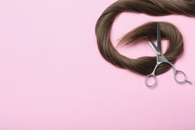 Photo of Professional hairdresser scissors and hair strand on pink background, flat lay with space for text. Haircut tool
