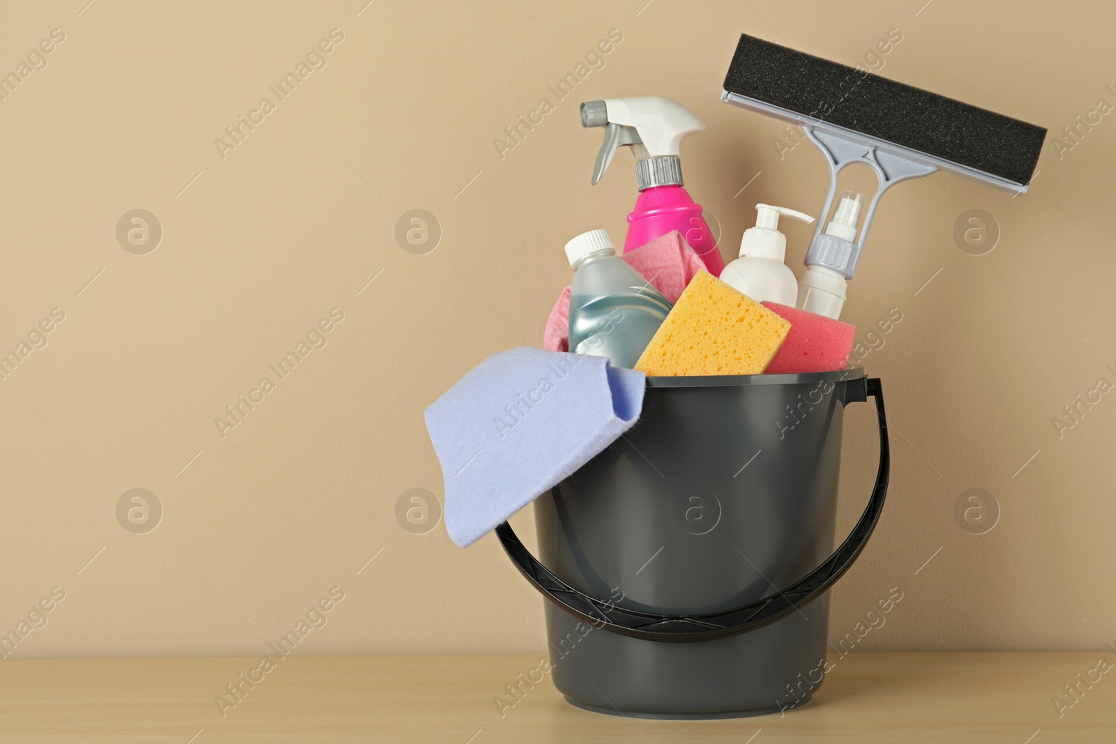 Photo of Bucket with different cleaning supplies on wooden floor near beige wall. Space for text