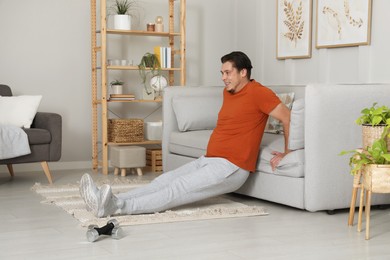 Photo of Overweight man doing exercise near sofa at home