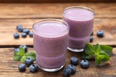 Photo of Glasses of blueberry smoothie with mint and fresh berries on wooden table