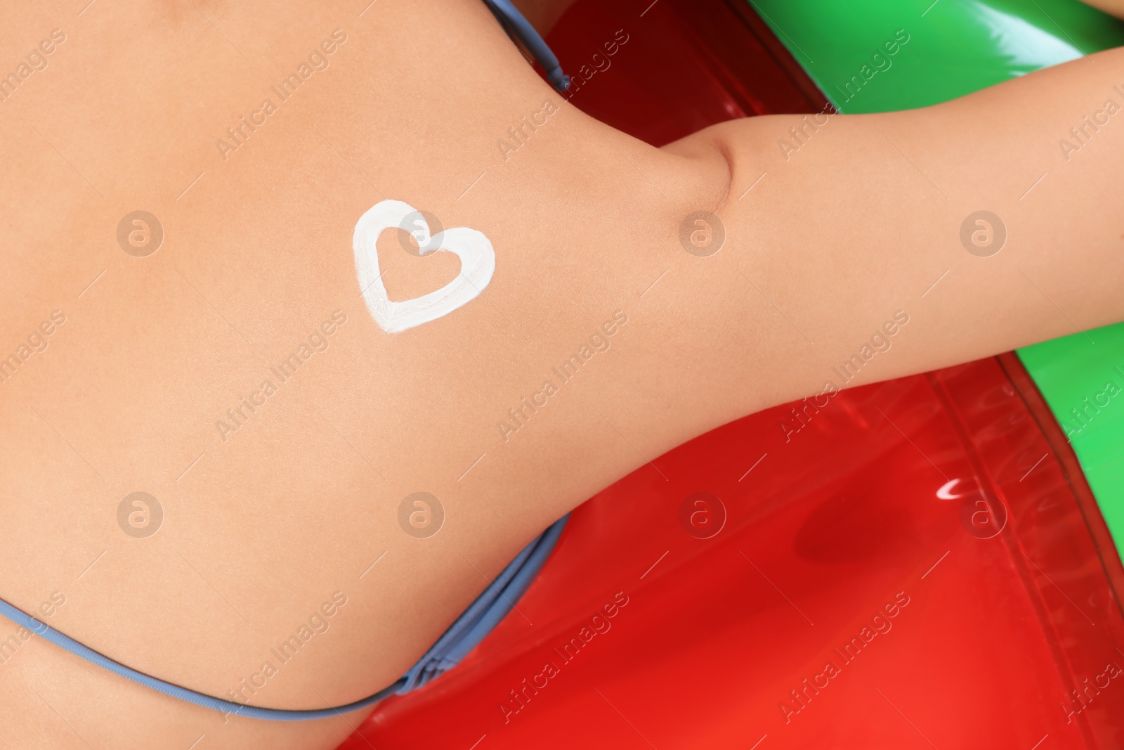 Photo of Young woman with heart drawn with sunscreen lying on inflatable mattress, closeup. Seasonal suntan