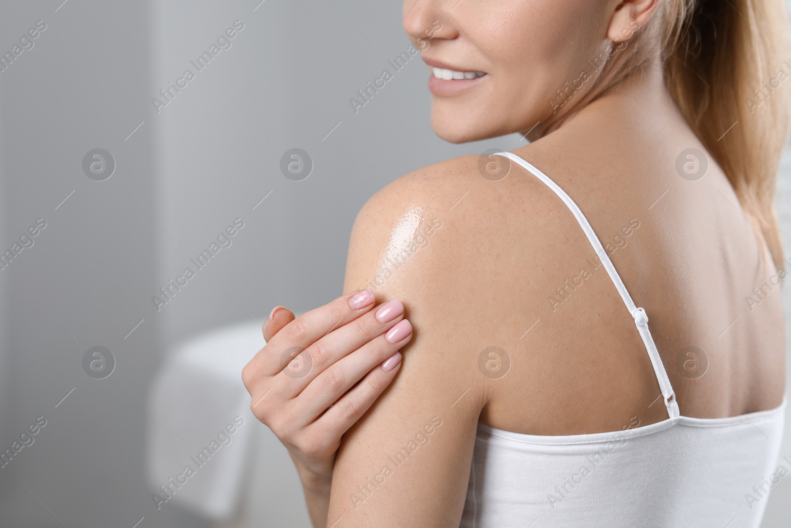 Photo of Woman applying body oil onto shoulder indoors, closeup. Space for text