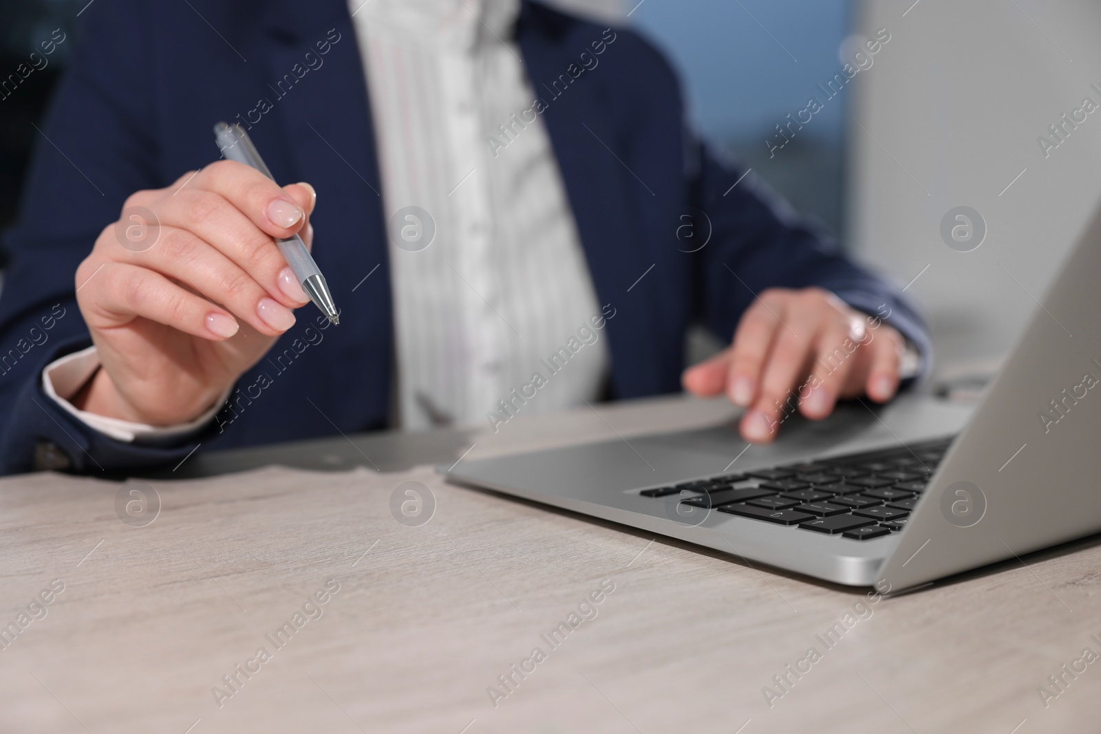 Photo of Woman with pen working on laptop at wooden table, closeup. Electronic document management